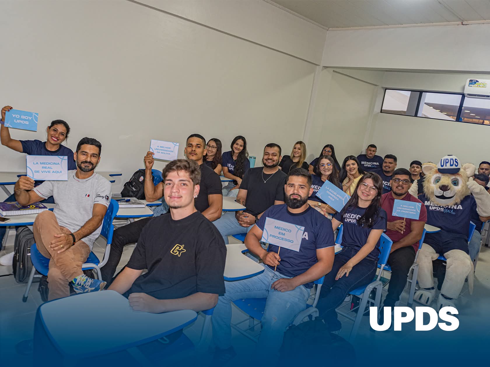 Salón de clases lleno de estudiantes con la mascota de UPDS Cobija